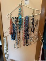 Photo of assorted colorful costume jewelry necklaces hanging on wire hangers against a peach wall.