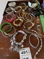 Photo showing a full assortment of various bracelets on a wooden surface including metal, resin, and colorful bangles, a charm bracelet and delicate link bracelets.