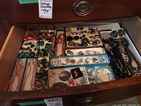 Wood drawer filled with compartmented boxes holding multiple jewelry pieces