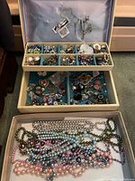 Overview of jewelry box interior compartments filled with assorted costume jewelry pieces.