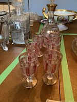 Photo showing vintage cranberry cut to clear decanter with stopper and six matching stemware glasses arranged on a table.
