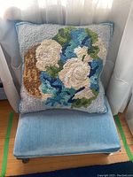 Footstool with pillow on top next to window.