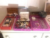 Overview of seven containers holding assorted costume jewelry items including necklaces, bracelets, pins, earrings