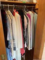 Photo of various ladies dresses, blouses, and sweaters hanging in closet on hangers.