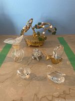 Overview of all six items on marble surface including Lalique perfume bottle, Swarovski figurines, and decorative jade tree