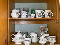 Shelf showing a variety of mugs including floral Sadler and Royal Windsor character mugs, and some clear glass mugs and beer glasses.