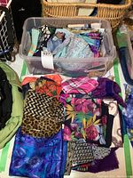 Plastic bin filled with colorful folded scarves, including various prints like animal, plaid, floral, and geometric