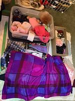 Photo showing folded colorful silk and polyester scarves, primarily in purples and pinks, with boxes of additional accessories and scarves nearby.