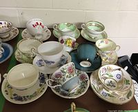Overall view showing eleven tea cups and saucers with diverse patterns and colors arranged together