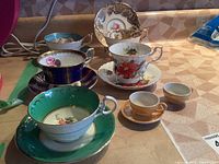Full view of six teacups and saucers arranged on a shelf showing variety of colors and designs