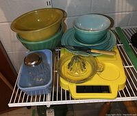 Photo showing a yellow mixing bowl with clear bottom, a blue Fire-King bowl, a yellow glass citrus juicer, and a vintage glass sugar pourer