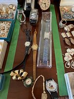 Overview photo showing multiple vintage ladies wristwatches including leather and metal bands, a small table clock, brooch watch, and a Mickey Mouse watch.