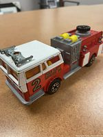 Side angle of red and white Majorette fire engine showing detailed roof equipment and yellow windows.