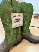 Photo showing pair of green and brown cowboy boots with white and brown decorative stitching and Justin Boots tag.