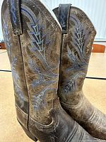 Side view of the pair of brown Justin cowboy boots showing detailed blue and tan leaf embroidery and pull tabs