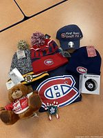 Photo of assorted NHL knit toques including Montreal Canadiens navy blue and red toques, Boston Bruins toque, a Detroit Red Wings teddy bear, a Montreal Canadiens insignia, a Toronto Maple Leafs pin, a First Round Draft Pick baseball cap, and NHL decals.