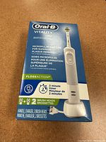 Box front showing Oral-B Vitality electric toothbrush features and contents including handle, charger, and 2 brush heads.