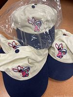 Photo showing several vintage Energizer Bunny hats with cream-colored tops, navy brims, and embroidered logos, some hats still in plastic wrapping.