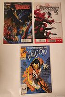 Photo showing three Marvel comics: The Falcon #1, Thunderbolts #1, and Avengers #2, all with detailed cover art.