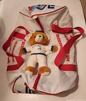 Full view of the Mr. Sub 10th Anniversary duffle bag with red straps and Toronto Blue Jays plush bear placed on top.