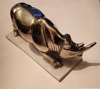 Front and side view of vintage stainless steel rhinoceros statue on marble base, showing polished metal surface and natural marble base.