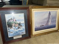 Two framed paintings side by side on floor, showing sailboat art and lighthouse art.