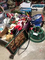 Full view of Christmas items including tree stand, assorted ornaments, wreaths, table runner, mugs, and blanket scattered on floor and inside containers