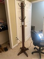 Full view of the vintage wooden coat tree standing upright next to a door and office chair.