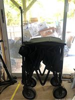 Side view of folded black collapsible wagon showing wheels and handle in storage position.
