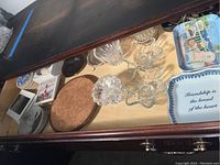 Photo showing various glass and crystal items, including crystal candle holders, coasters, and decorative plates inside a drawer.
