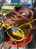 Photo showing several coiled heavy-duty extension cords in orange and yellow on a barrel, with part of a power strip visible.