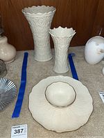 Two vases and serving plate with bowl arranged on floor in front of wooden cabinet