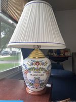 Full view of lamp showing floral porcelain base with Maryland label and pleated shade with blue trim.