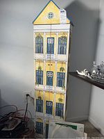 Photo of tall painted wooden media shelf shaped like a yellow house with blue accents