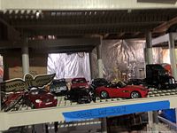 Overview of the assorted model cars displayed on a shelf including a red convertible and black semi-truck