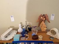 Full display of lot showing various bone china dishes, several decorative perfume bottles including blue glass and milk glass, a wood carved angel figurine, trinket boxes, and a porcelain clock.