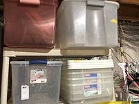 Shelving unit with four plastic storage containers; pink translucent containers stacked on top left, large clear container with blue handle below, two clear containers with white lids stacked on right