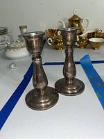 Pair of sterling silver candlesticks displayed upright on a surface with china in background.