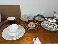 Overview of all six teacup and saucer sets on wooden surface showing variety of patterns and colors