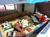 Photo of table with various model train buildings and parts including barn, houses, and building components scattered and showing some damage.