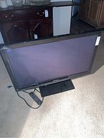 Full view of Panasonic 42 inch plasma TV on carpet floor with remote beside it.