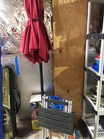 Red umbrella folded and tied with strap, stored in basement against wall with shiny insulating foil