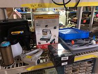 Paint sprayer and painting accessories on a metal rack including the Wagner Power Painter, trays, rollers, and an electric stapler.