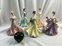 Overview of all five pastel-gowned figurines with green apple for scale