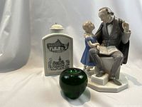 Overall view showing the three objects: the lidded tea caddy decorated with Danish buildings, the Bing Grondahl figurine of the older man and young girl, and a green apple size reference.