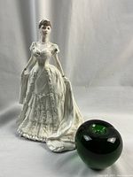 Front view of the bone china Queen Mary figurine alongside a green glass apple used for size reference.
