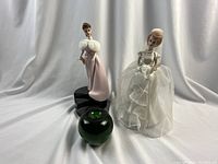 Two Enesco musical figurines with a green apple for size reference. Brides Dream in pink gown on black base and Enchanted Evening bride in white dress.