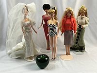 Five Barbie dolls standing with a green apple for size reference, including a wedding Barbie, Bubblecut doll, and others in vintage and handmade outfits