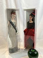 Overview of both dolls in clear display cases with green apple size reference