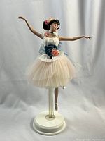 Front view of Prima Ballerina Barbie doll in tutu and floral hair adornments, displayed on clear stand with white base.